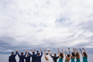 Guests on the wedding celebration are standing on the river quay, holding their hands up and looking in to the distance.